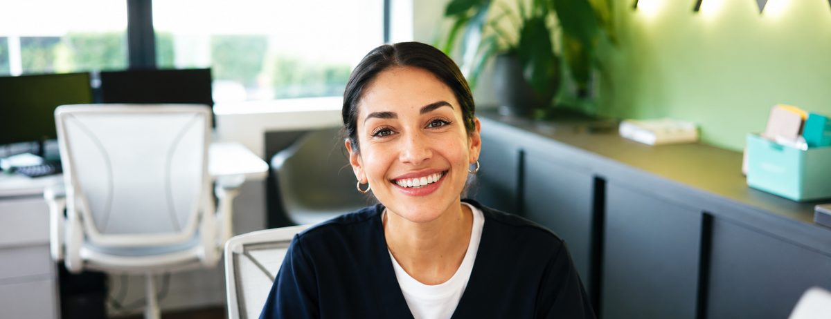 A clinic receptionist smiling at the front desk of a medical office.
