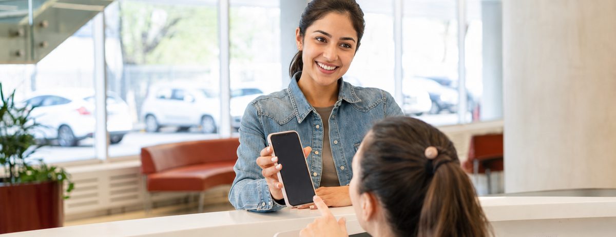 A patient at the front desk showing her phone to the receptionist.